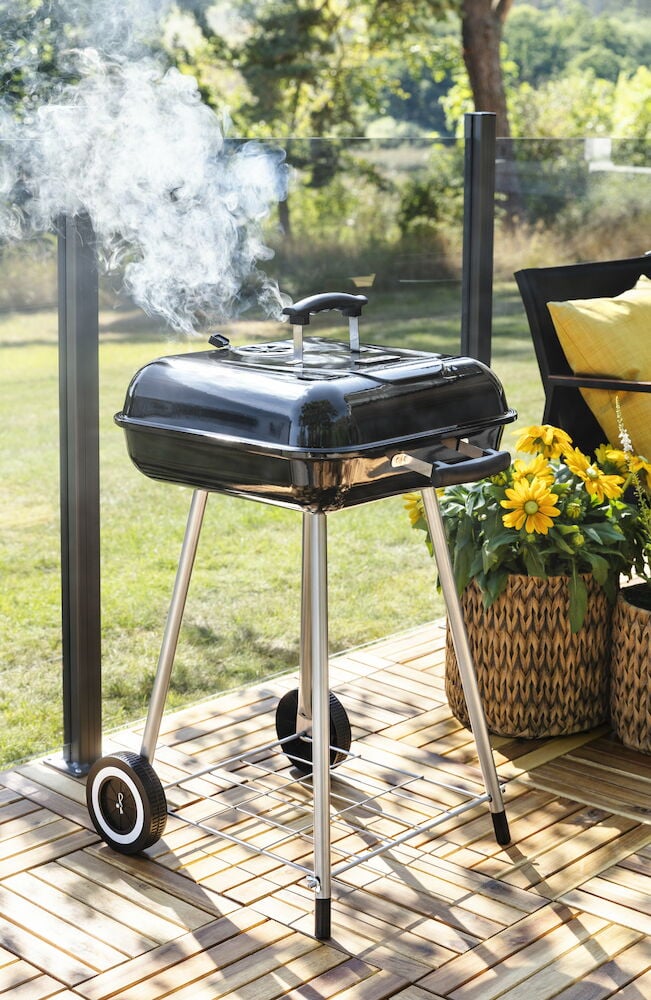 Svart liten kolgrill på ben med lock och hjul.