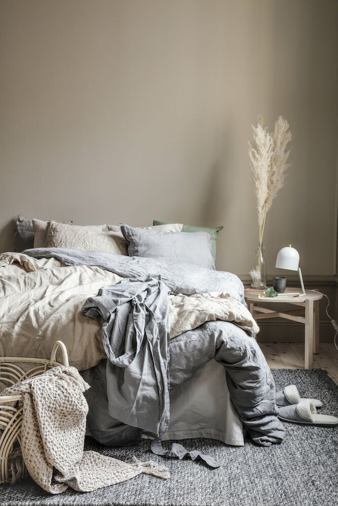 Tummanharmaa käsinkudottu matto sängyn alla makuuhuoneessa.