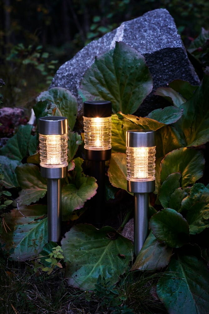 Drei solarbetriebene Gartenlampen aus Kunststoff zwischen grünen Blättern.