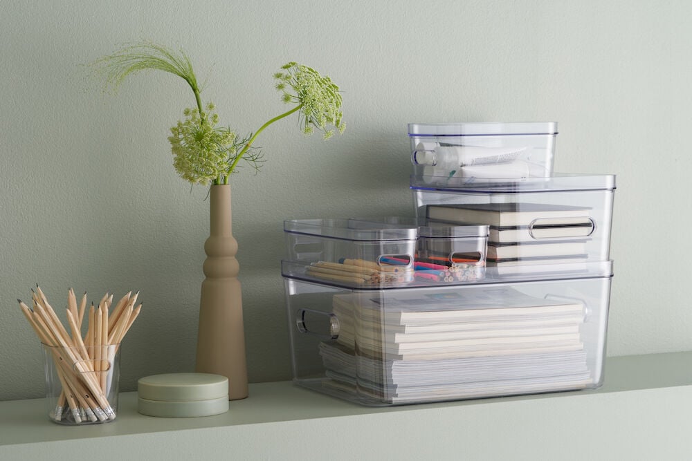 Tre genomskinliga förvaringslådor staplade med kontorsmaterial.