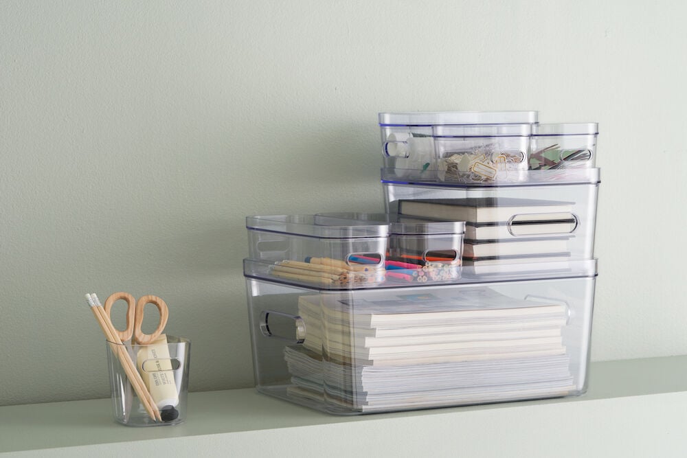 Flera transparenta förvaringslådor med kontorsmaterial och böcker.