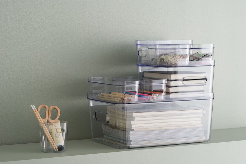 Tre genomskinliga förvaringslådor med kontorsmaterial och anteckningsblock.