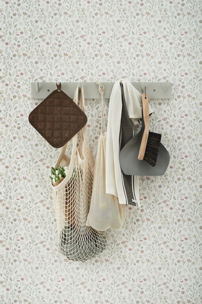 Ljusgrå krokbräda med köksartiklar mot blommig tapet.