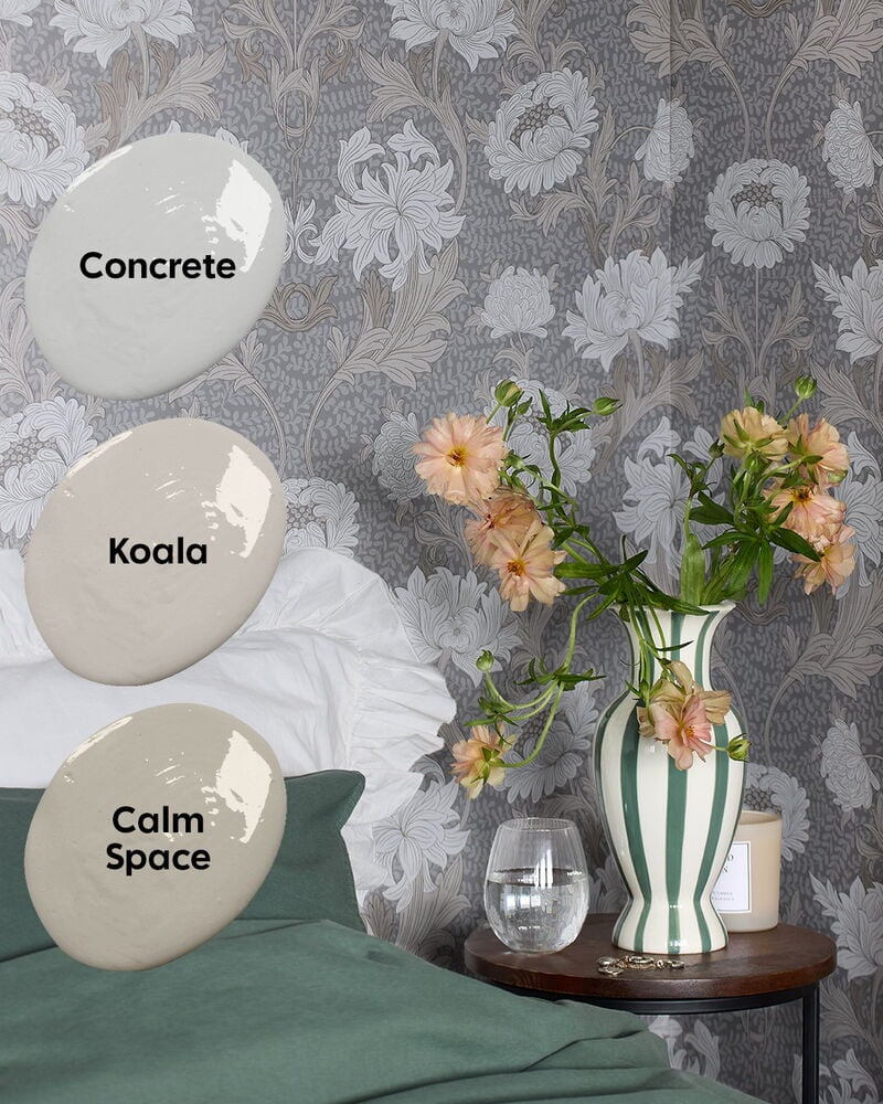 Grå mönstrad tapet med blommor bakom säng och vas.