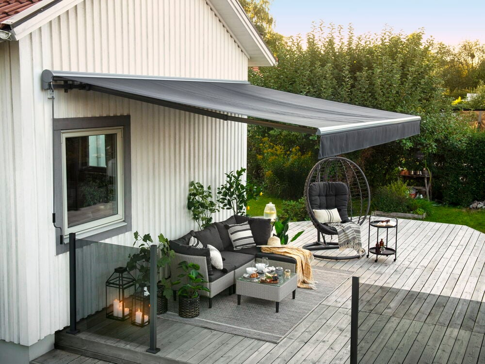 Grå terrassmarkise montert over uteplass og utemøbler.