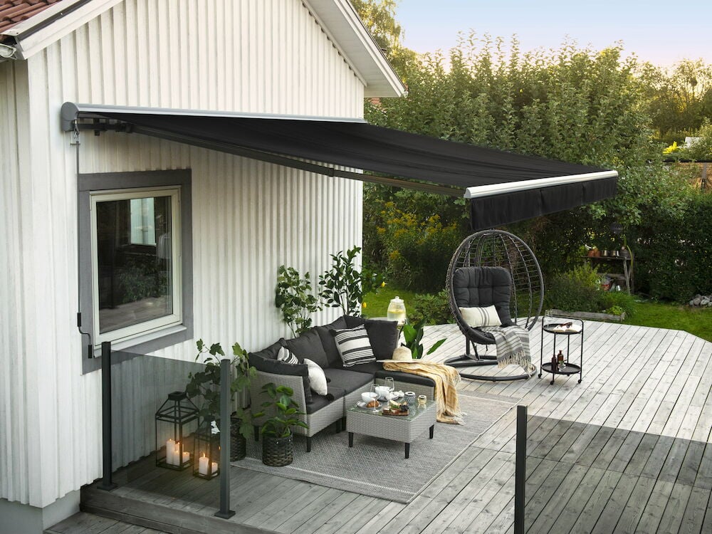 Svart terrassemarkise over uteplass med hagemøbler.