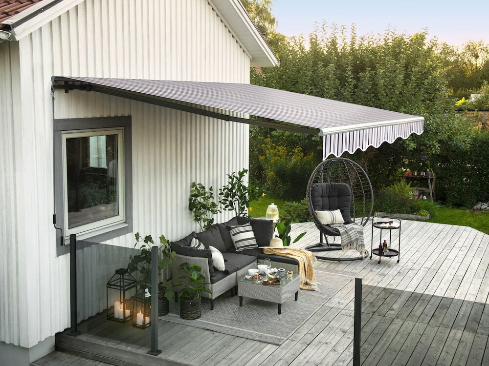 Gråvit terrassmarkis monterad över trämöblerad altan.