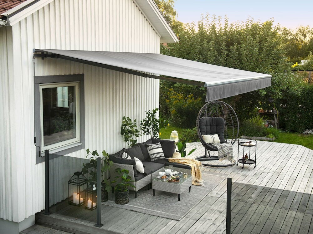 Ljusgrå terrassmarkis monterad över möblerad altan.