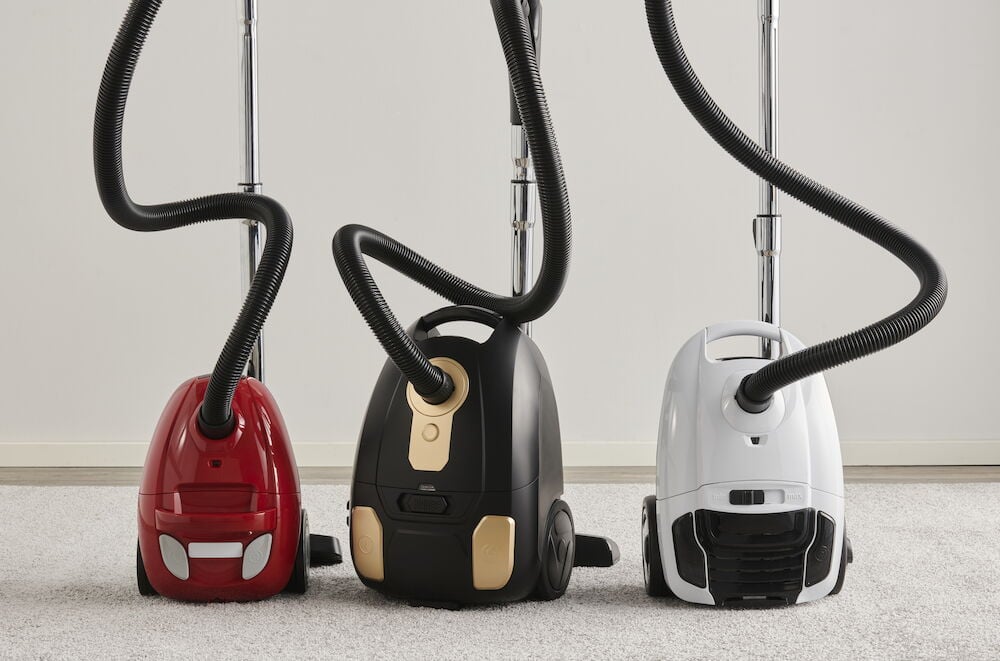 Tre dammsugare i olika färger på golvmatta.