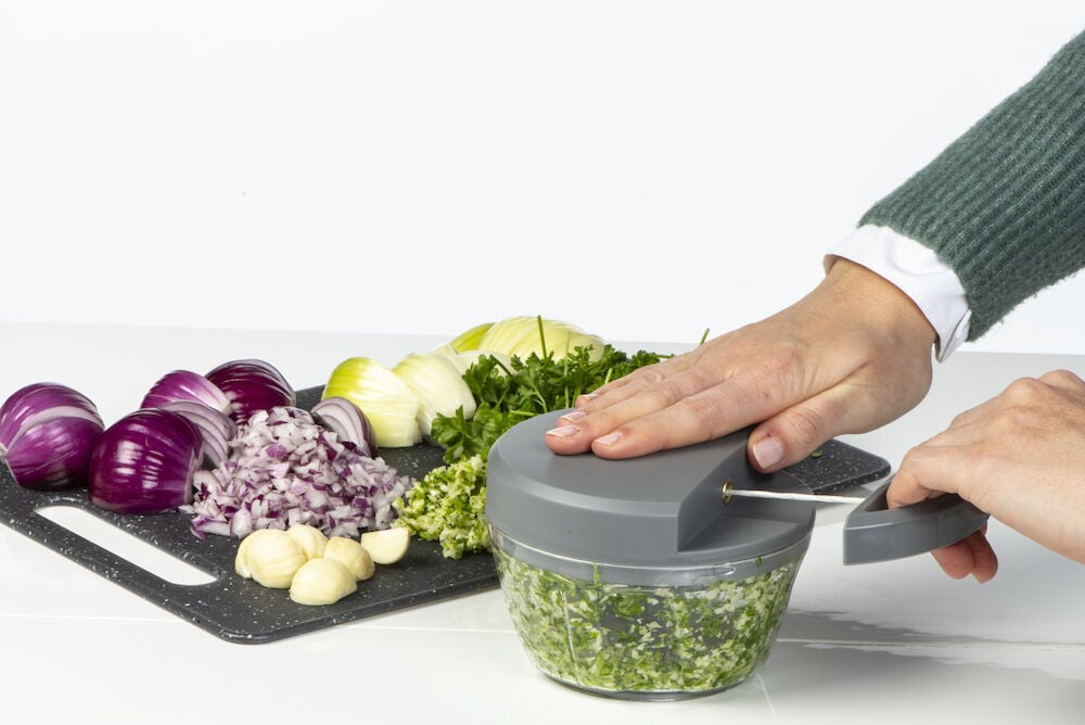 Manuell minihackare hackar grönsaker på köksbänk.