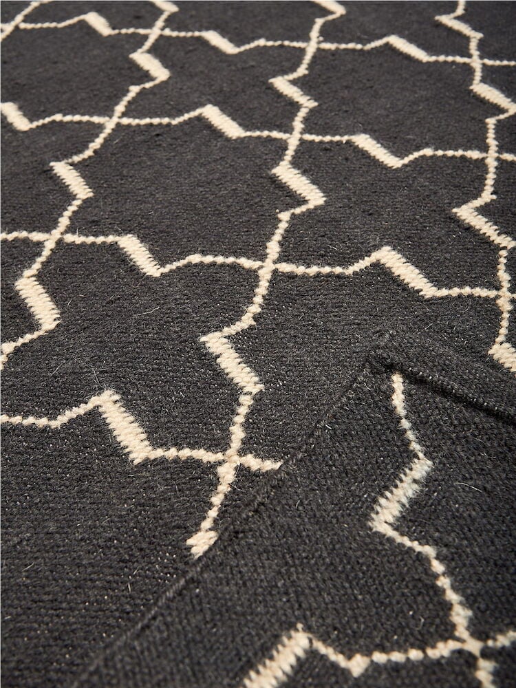Tummanharmaa villamatto, jossa valkoinen geometrinen kuvio.