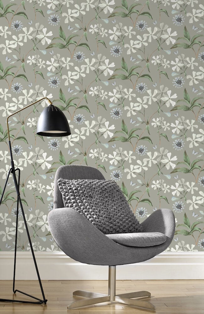 Grå tapet med vitt blommönster bakom grå fåtölj.