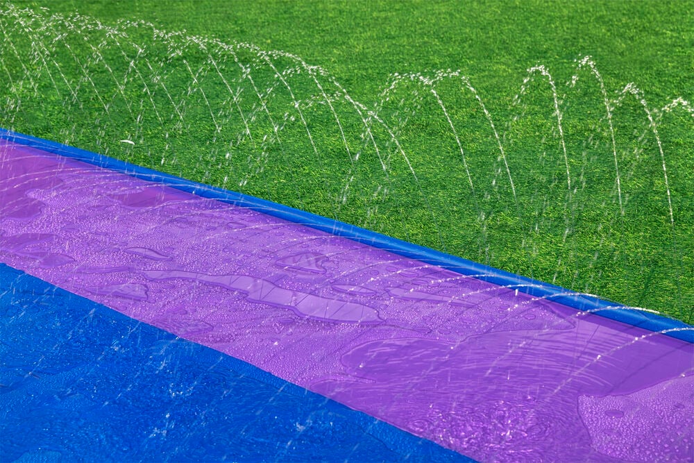 Lila vattenglidbana med sprinklers på gräsmatta.