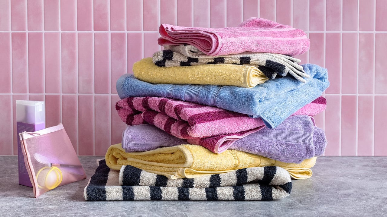 Fargerike håndklær i en haug foran en rosa flisvegg.