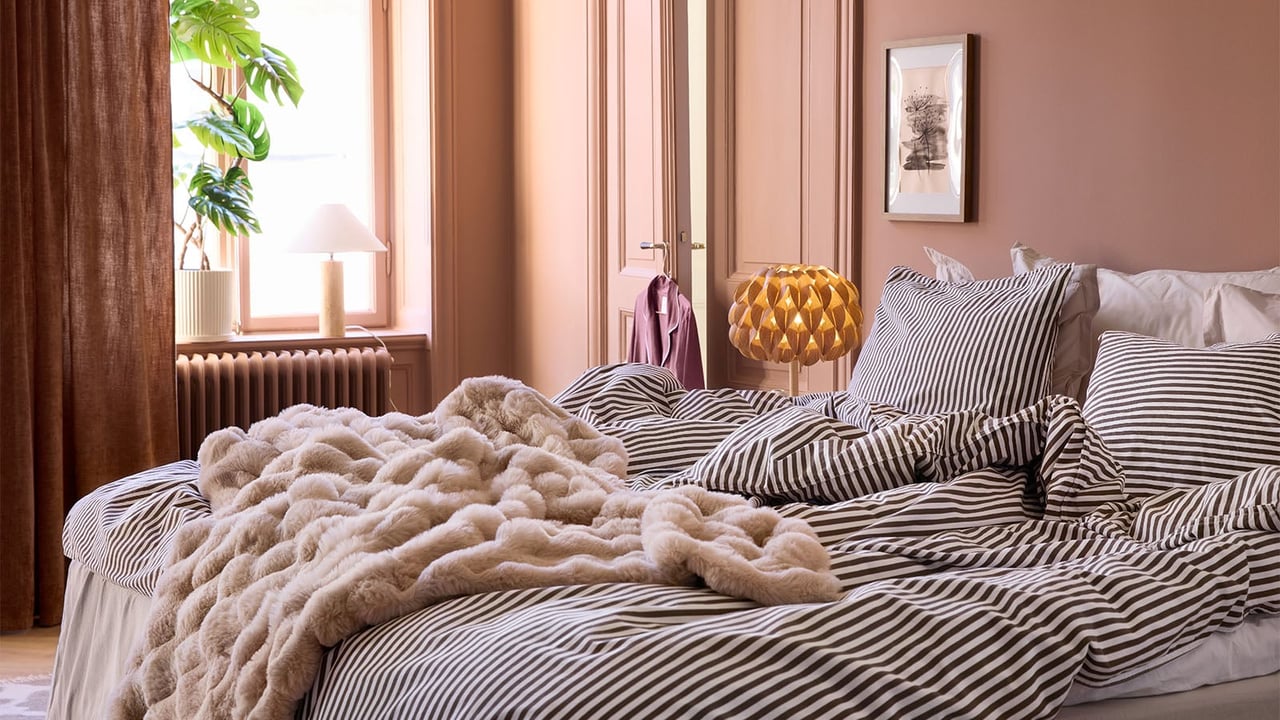Et soverom med terrakottafargede vegger, stripete sengetøy og et mykt, beige pledd.
