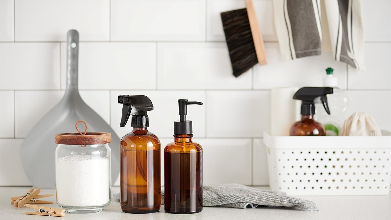 Suihkepullo ja saippua-annostelija ruskeaa läpinäkyvää muovia penkillä valkoisen laattaseinän edessä.