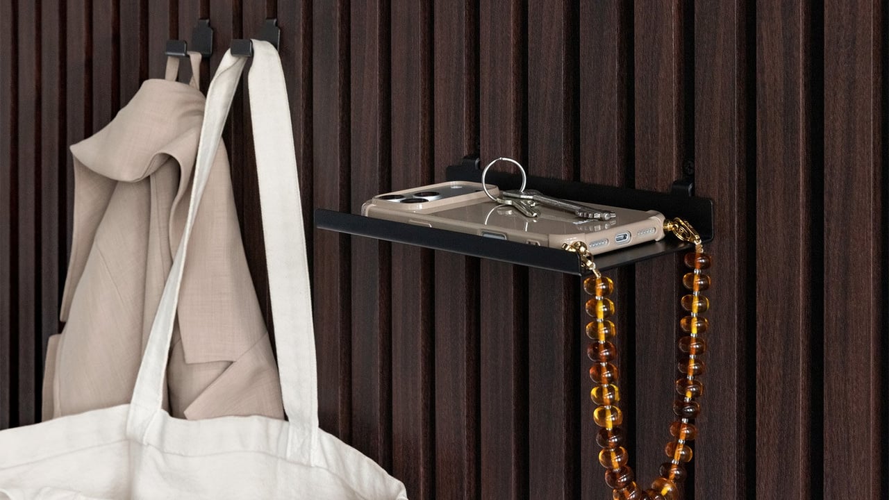 Matkapuhelin on pienellä hyllyllä, joka on kiinnitetty tummaan akustiikkapaneeliin.