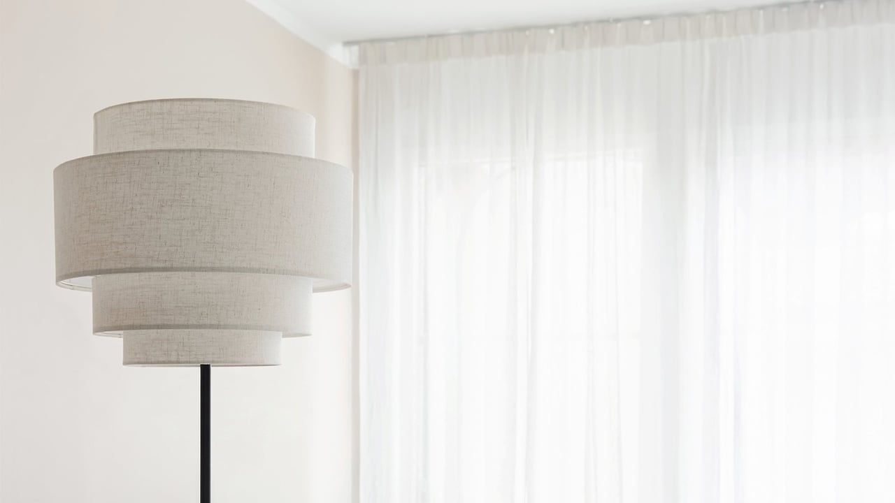 Ohuet valkoiset verhot, jotka on ripustettu kattokiinnityksellä valoisassa olohuoneessa.