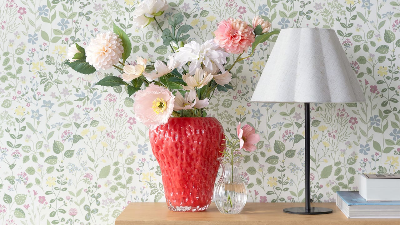 Röd jordgubbsformad vas med bukett av konstblommor i rosa och vitt.