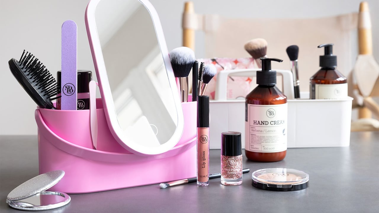Rosa beautyboks med speil fylt med skjønnhetsartikler som sminkebørster og neglefil.