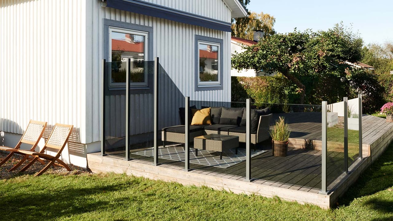 Puuterassi valkoisen omakotitalon edessä, jota ympäröi sävytetty lasikaide.