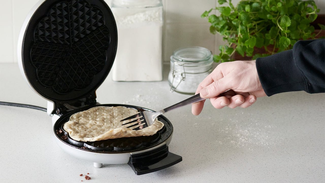 Käsi, joka kääntää vohveliraudalla vohvelia haarukalla.