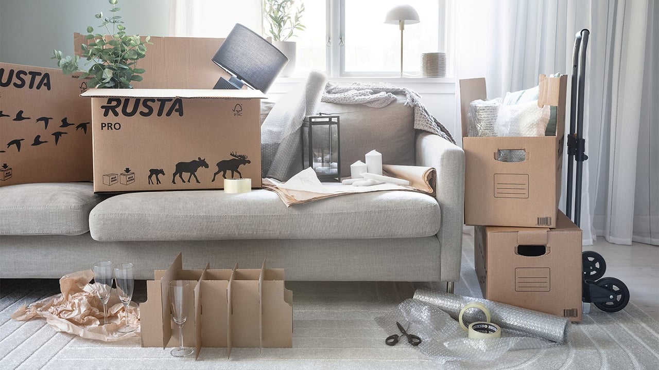 Flyttkartonger staplade på golv och i en soffa med en pirra och packmaterial vid sidan om.