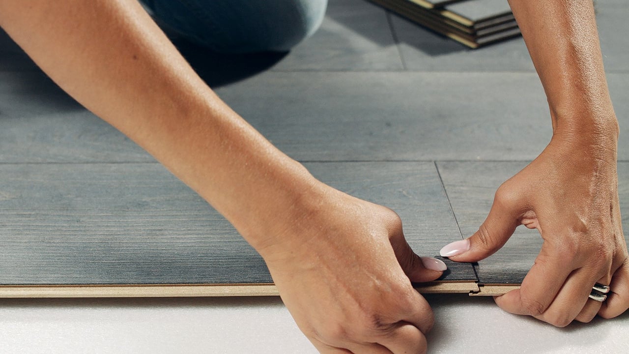 Nærbilde av person som legger laminatgulv i gråtonet tre.