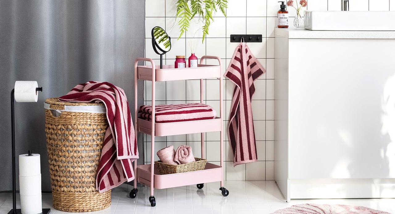 Bad med dusjforheng, badematte, skittentøykurv, håndklehenger og rullevogn.