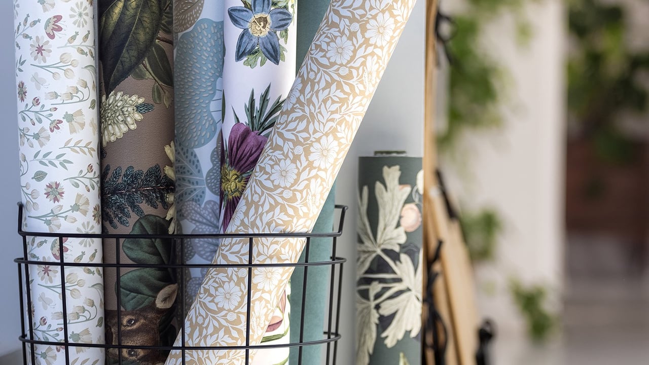 Eri värisiä ja kuviollisia tapettirullia mustassa lankakorissa.