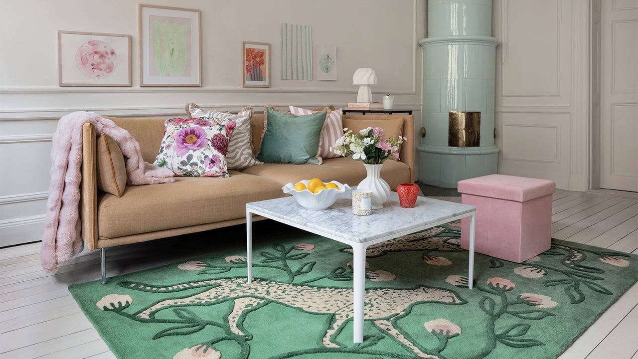 Kevään väreillä sisustettu olohuone. Vihreä matto, jossa on kissaeläimiä, kehystää ruskeaa sohvaa ja marmorista sohvapöytää.