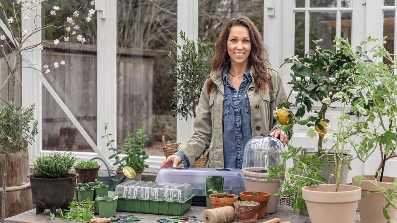 Influenseren Sofia Björk står foran et plantebord med dyrkingstilbehør i et drivhus.