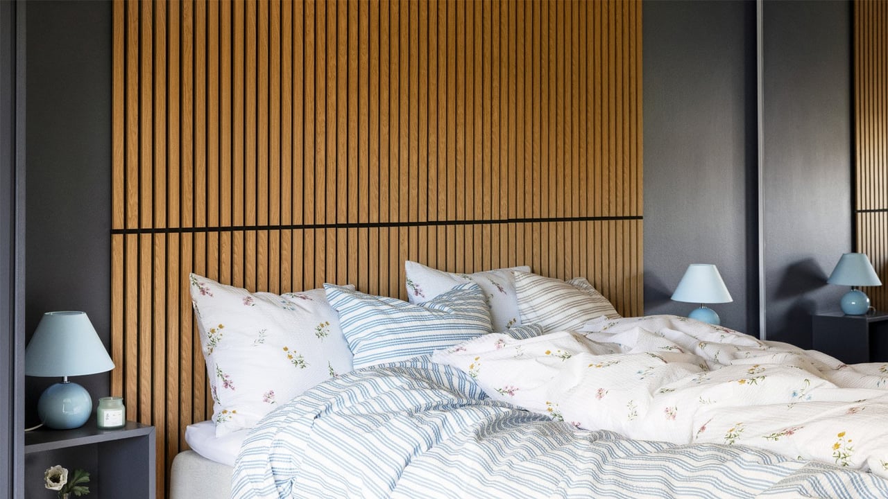Bäddad dubbelsäng i ett sovrum med akustikpaneler i trä som sänggavel.