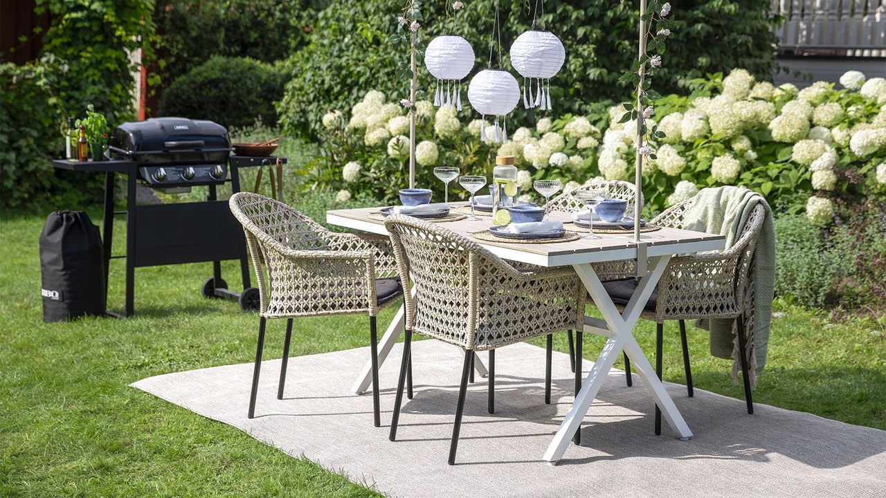 Ett dukat bord pyntat med hängande solcellslampor över i en lummig grön trädgård.