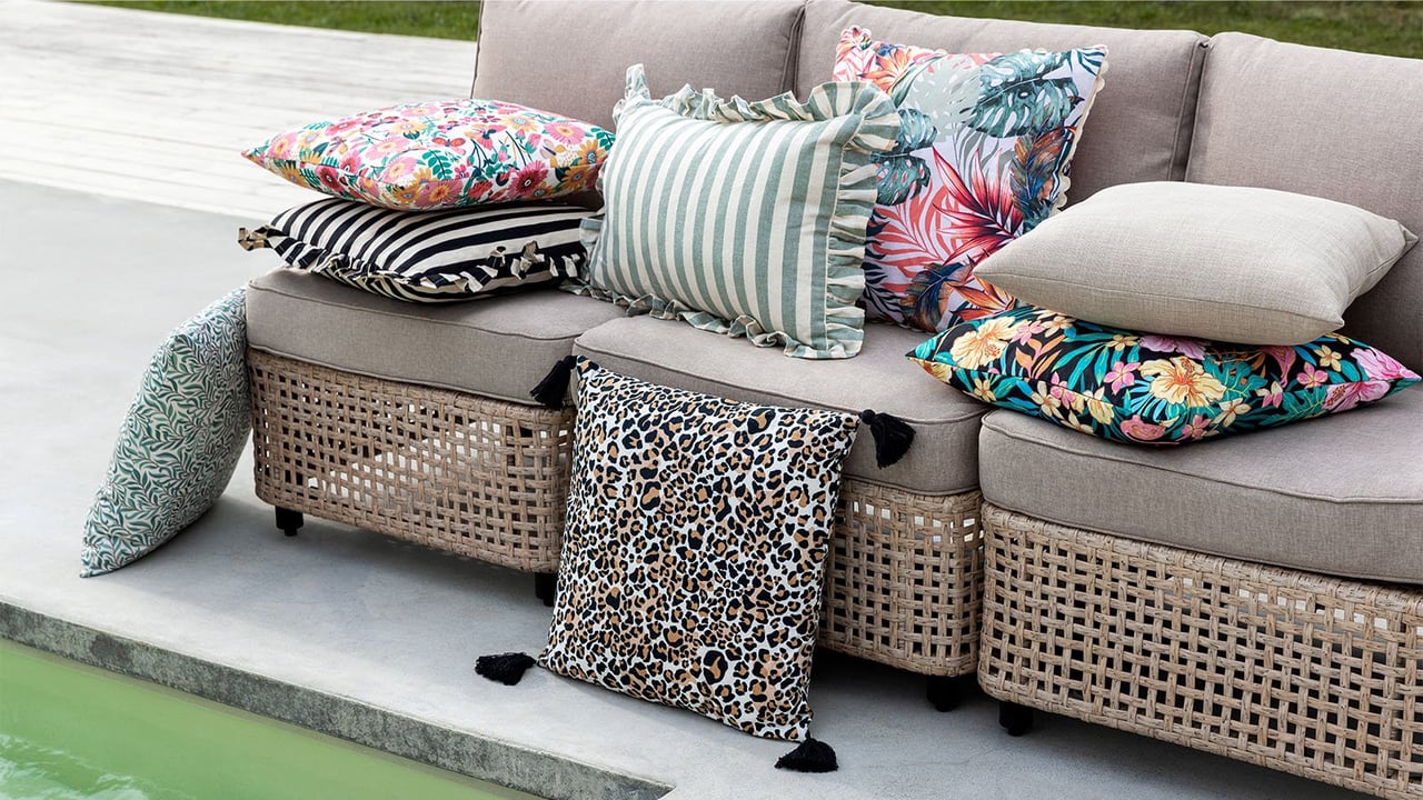 Utekuddar i olika mönster och färger ligger i en loungesoffa intill en pool.