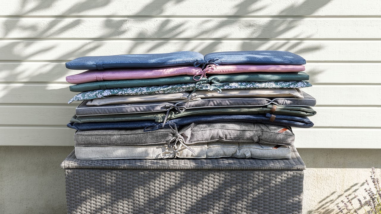 Staplade sittdynor i olika färg och form ligger på en förvarings- och dynlåda utomhus.