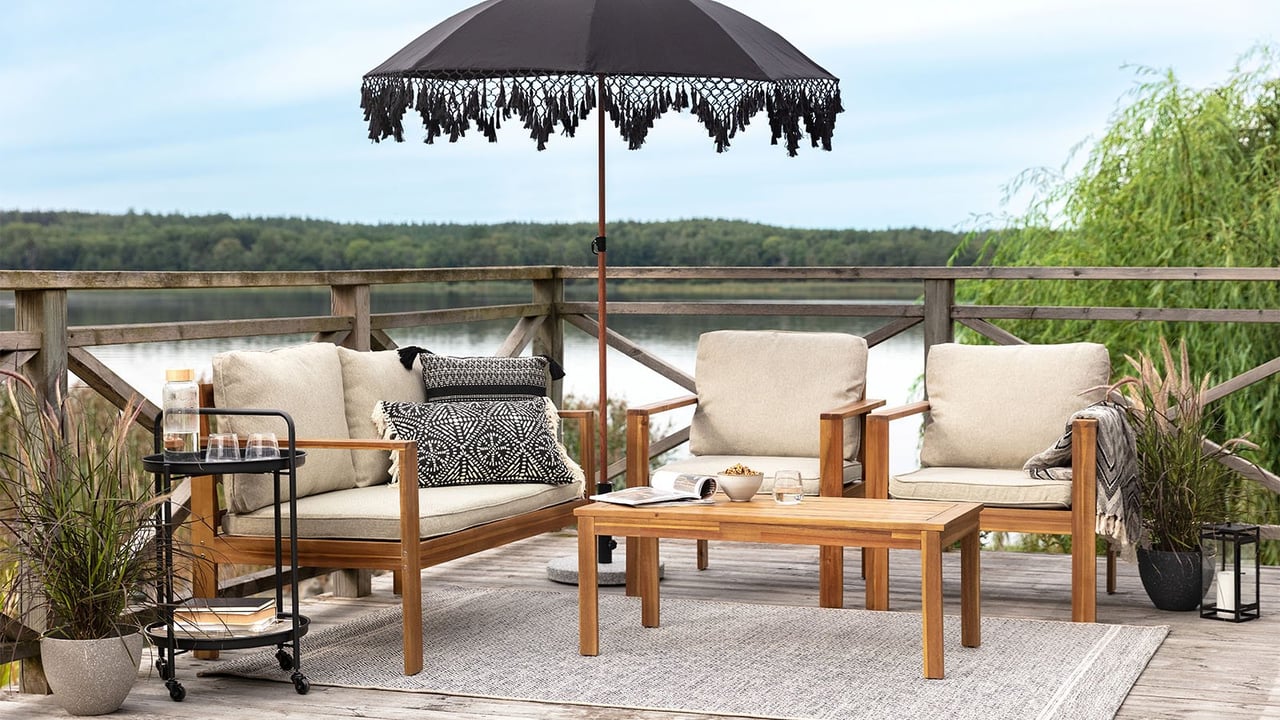 Loungegrupp i trä med beige dynor på stor terras med utomhusmatta och svart parasoll.