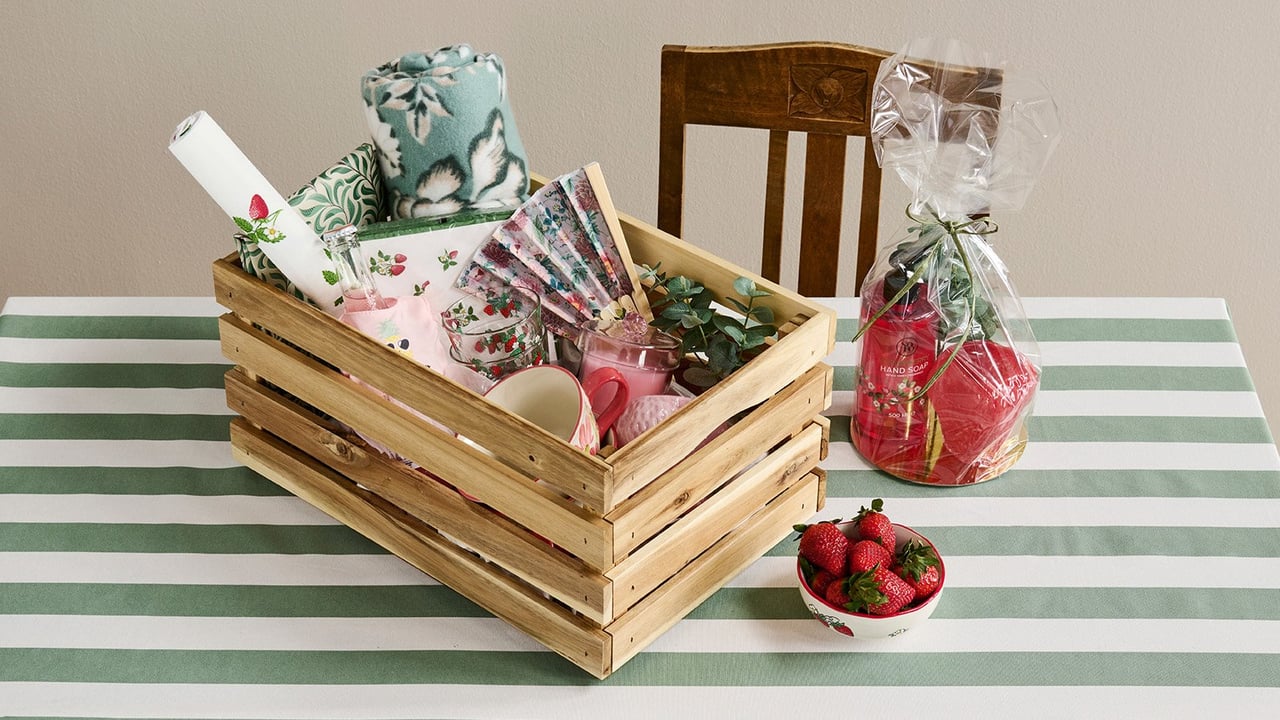 Trälåda med pläd, servetter, muggar, duk, solfjäder och cellofanpåse.