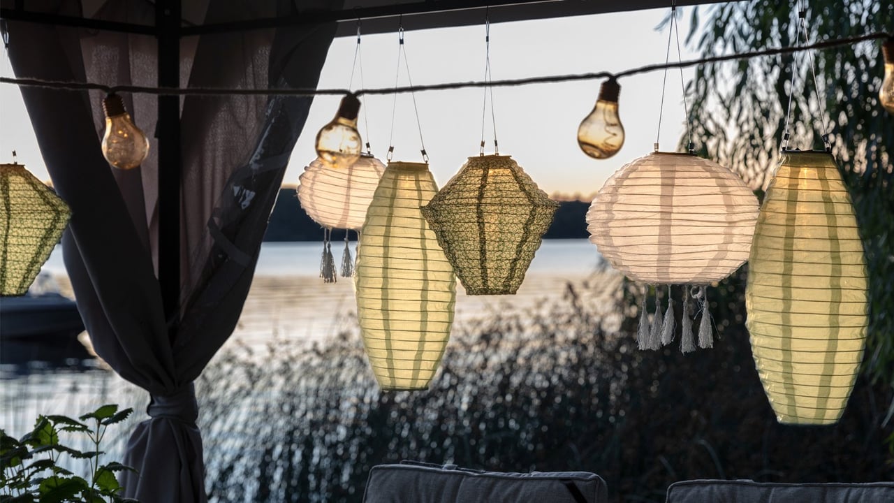 Stimmungsvolle Terrasse am Wasser in der Abenddämmerung, dekoriert mit beleuchteten Reispapierleuchten und Lichterketten für einen gemütlichen Sommerabend.