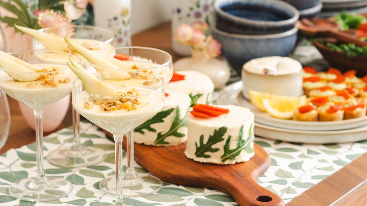 Katettu pöytä, jolla on tarjolla pikkupurtavaa, kuten pannacotta lasissa, voileipäkakku ja krustadeja.