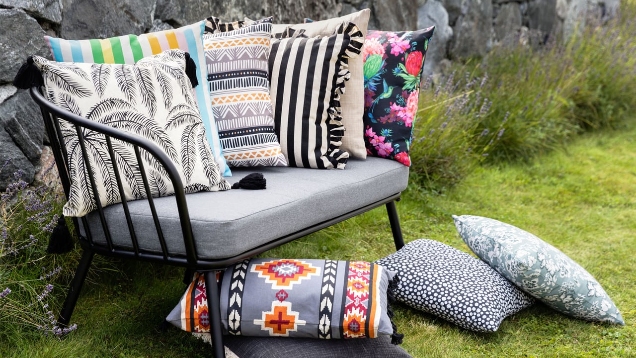 Loungesofa med uteputer i blandede mønstre og farger på en plen i en hage.