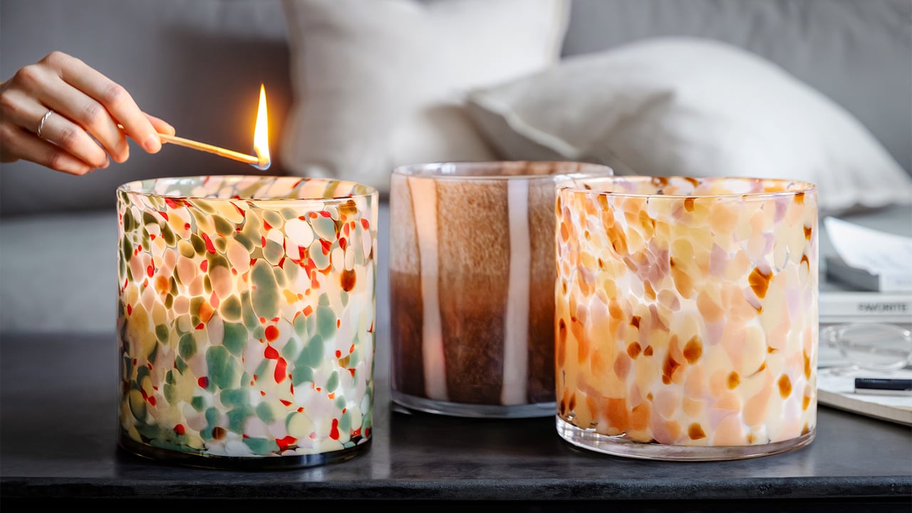 Hand, die eine Kerze in einem gepunkteten Teelichthalter auf einem Wohnzimmertisch anzündet.