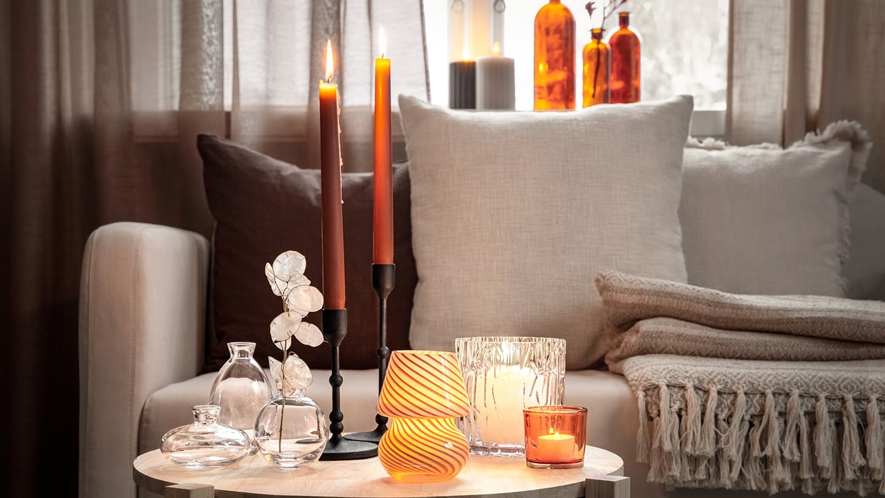 Gemütliche Sofaecke mit angezündeten Kerzen, Decken und dekorativen Glasvasen auf einem runden Tisch.