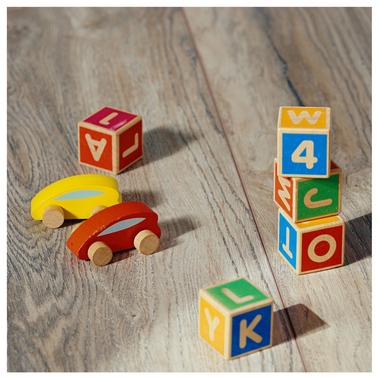 Närbild på ett laminatgolv med leksaksbilar och byggklossar utplacerade på ytan.