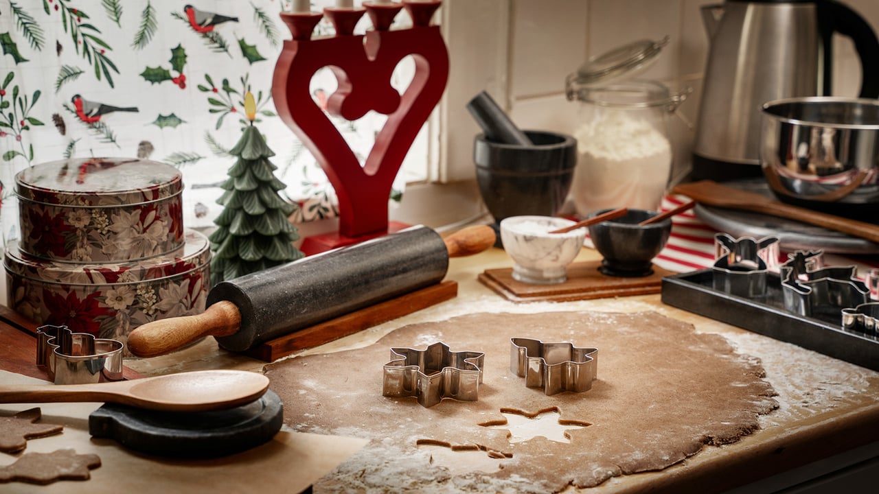 En utkjevlet pepperkakedeig med kjevle og pepperkakeformer. En adventsstake i bakgrunnen.