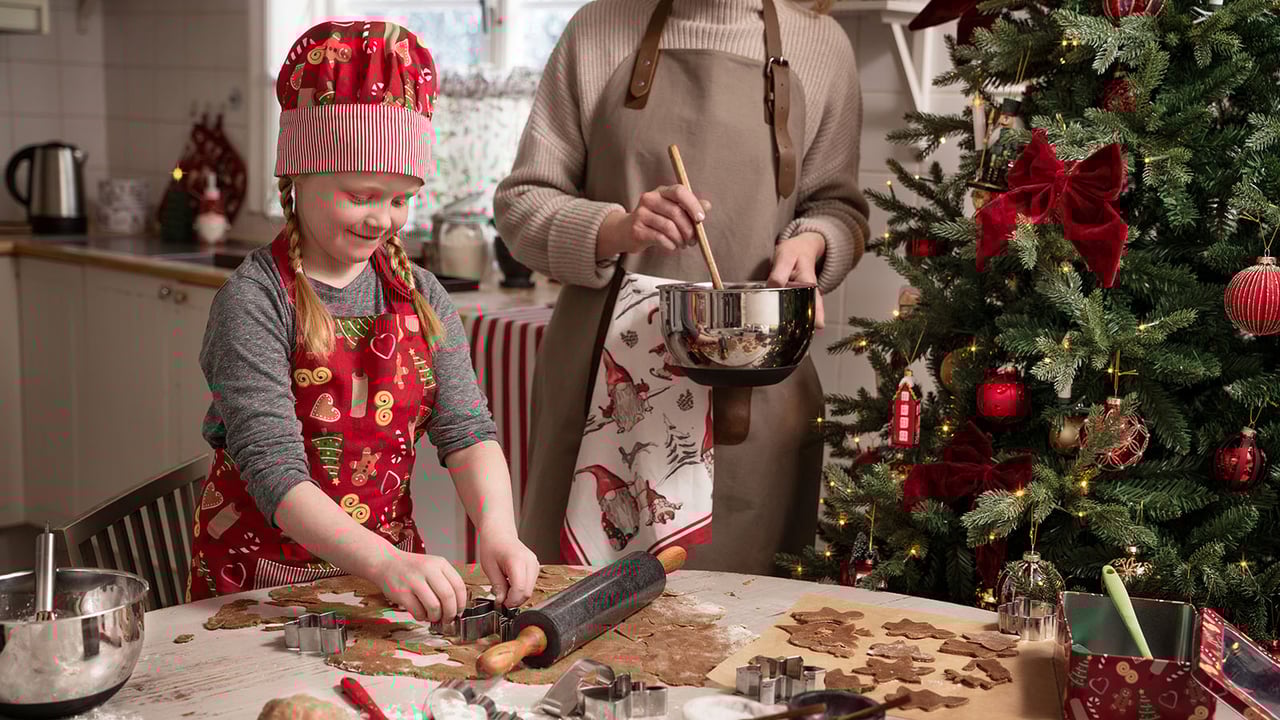 Jouluiseen esiliinaan pukeutuneet lapset painavat piparkakkuja taikinasta muoteilla.
